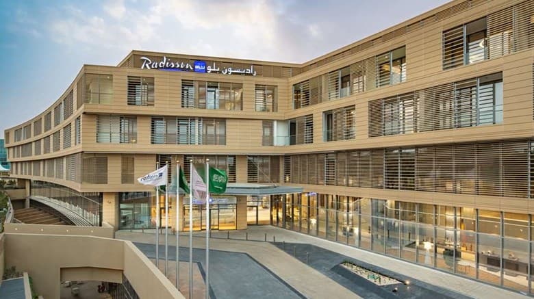 The terra cotta stone facade of the Radisson Blu Riyadh Diplomatic Quarter glowing during golden hour, framed by hanging gardens.