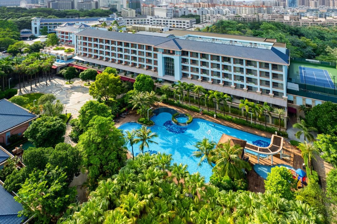A lush outdoor tropical pool deck at the Dongguan Marriott Hotel surrounded by palm trees and low-rise heritage architecture at the foot of Mount Qifeng.