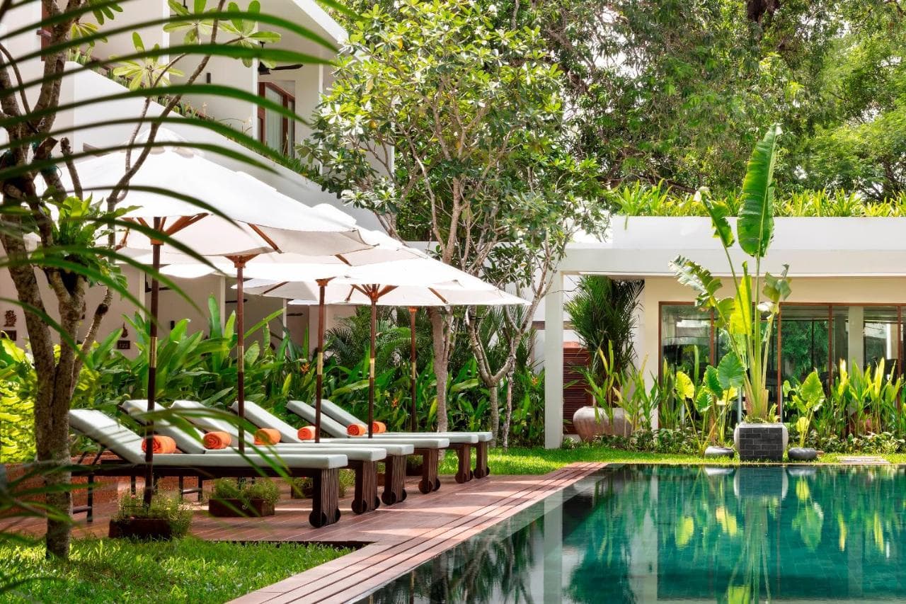 The Scribe Bar terrace at FCC Angkor by Avani at dusk, illuminated by warm lanterns under an ancient banyan tree.