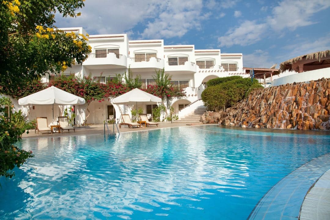 White arched colonial architecture of Iberotel Palace framing a calm blue lagoon pool and the Red Sea beyond.