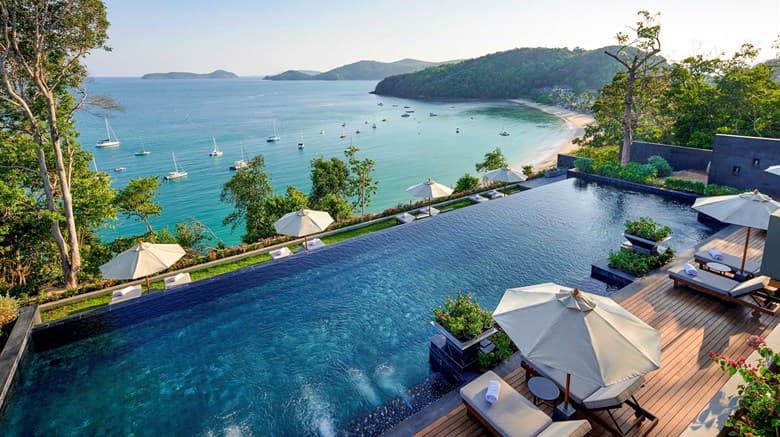 A dramatic, geometric infinity pool at V Villas Phuket merging with the Andaman Sea at twilight, viewed from a floating walkway.