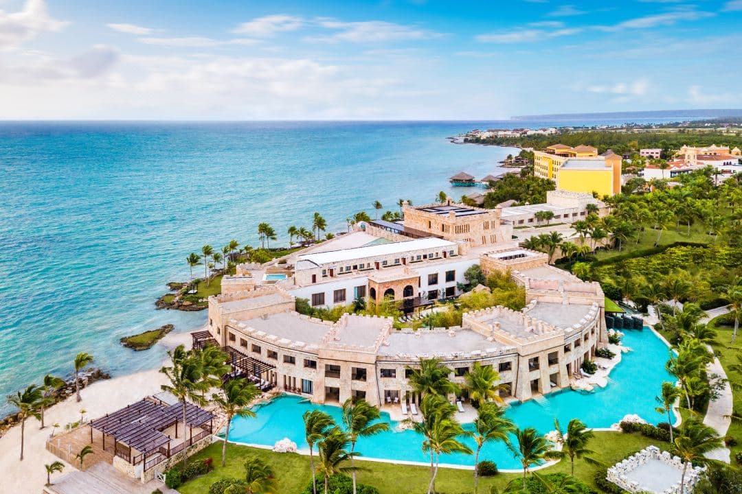 A dramatic stone fortress resort perched on a cliff overlooking the turquoise Caribbean sea, with an infinity pool blending into the horizon.