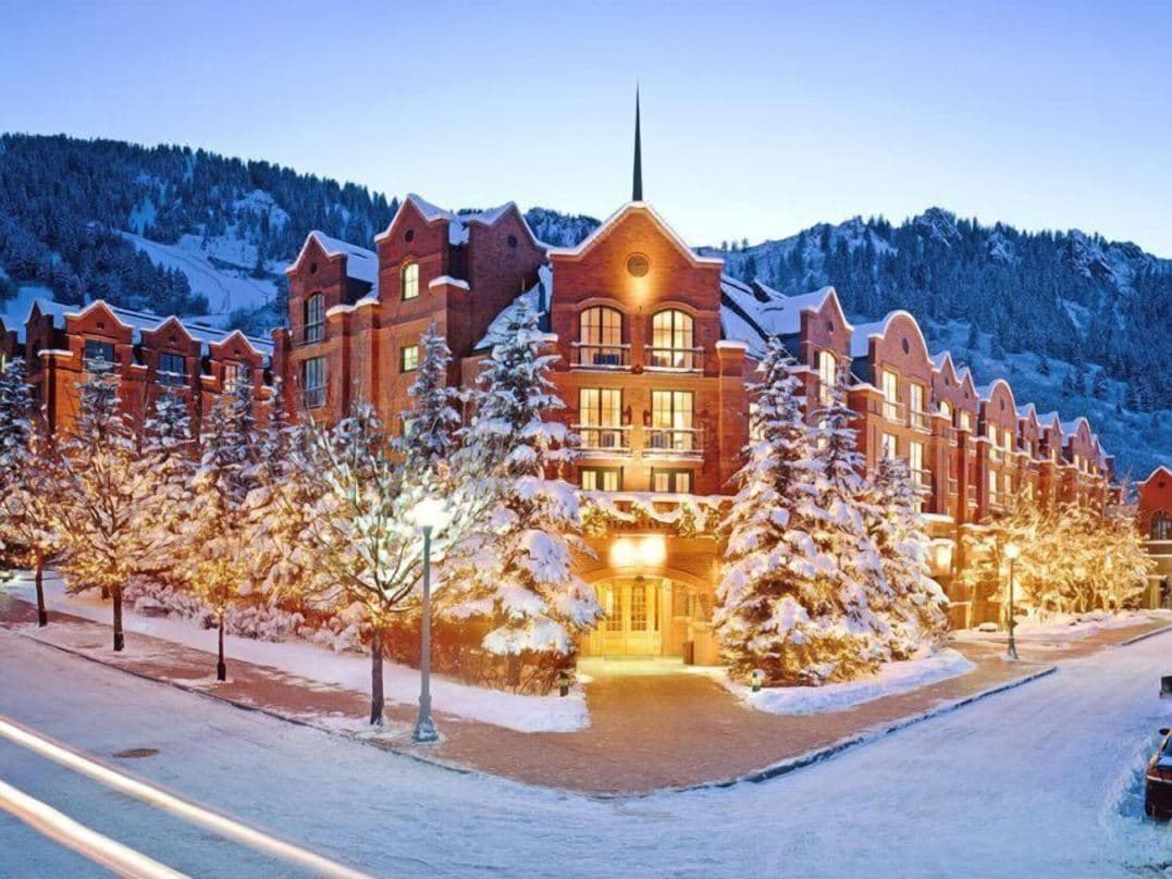 Steam rising from the St. Regis Aspen outdoor heated pool with snow-covered evergreens and the red brick manor facade in the background.
