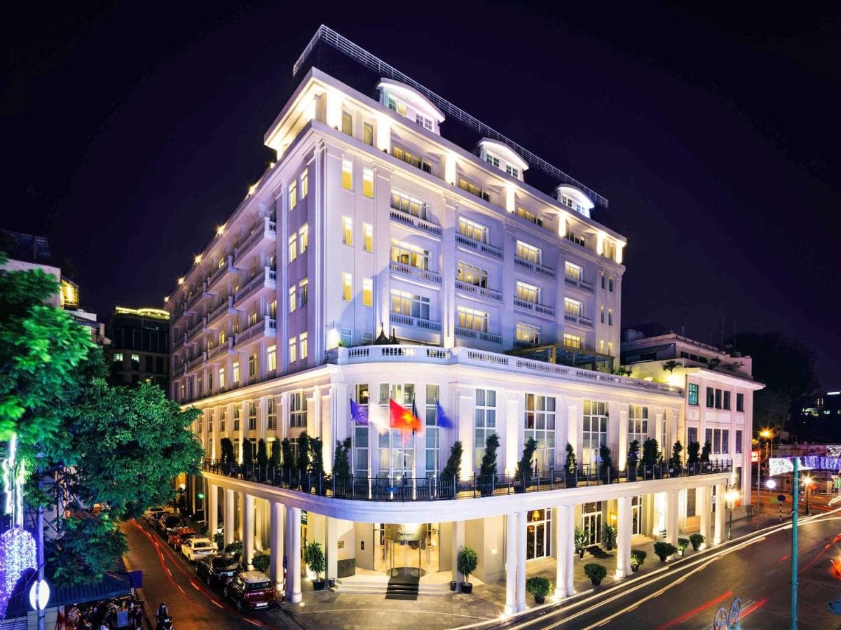 A dramatic hotel atrium with a glass dome ceiling, checkered floors, and theatrical velvet furniture at Hotel de l'Opera Hanoi.