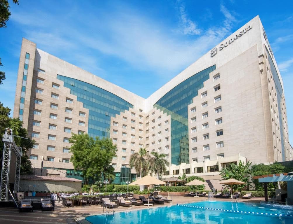 The illuminated outdoor swimming pool at Sonesta Cairo at twilight, framed by palm trees and the hotel's white multi-story facade.