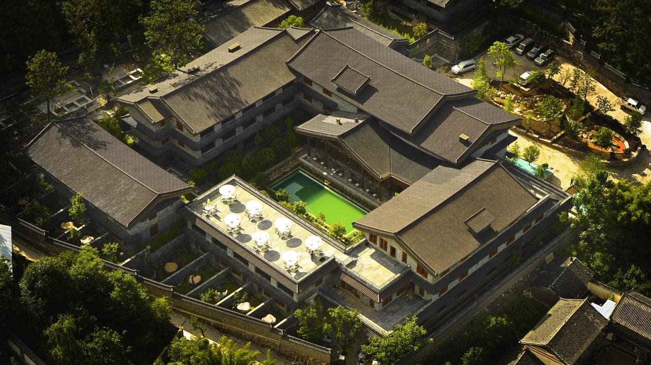 A traditional Naxi-style building at Songtsam Linka Lijiang with a heated outdoor pool reflecting the snow-capped Jade Dragon Snow Mountain.