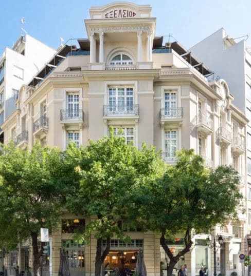 The Excelsior Thessaloniki's neoclassical facade illuminated at twilight, featuring arched windows and wrought-iron French balconies.