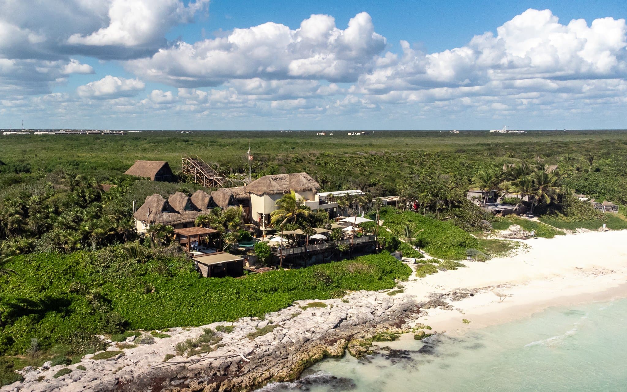 A cantilevered wooden terrace at Mezzanine Tulum overlooking turquoise Caribbean waters with a hammock swaying in the breeze.