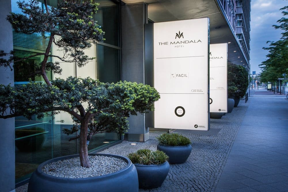 The bamboo-lined courtyard of FACIL restaurant at The Mandala Hotel, featuring glass walls and modern table settings.
