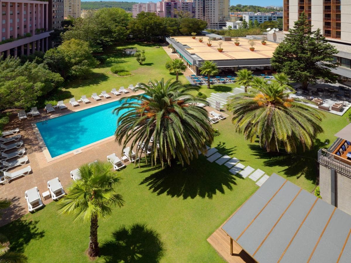 A large, kidney-shaped outdoor swimming pool surrounded by mature palm trees and sun loungers at the Lisbon Marriott Hotel.