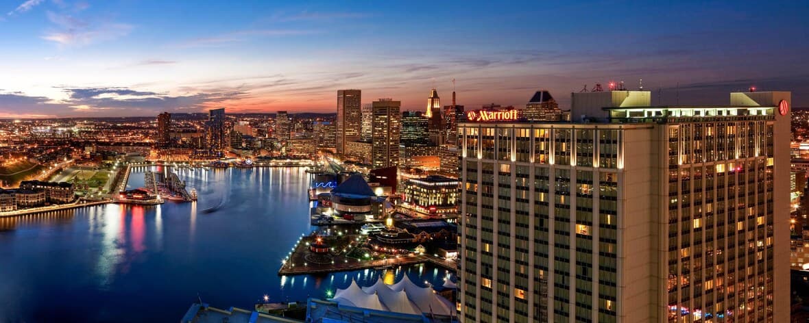 A high-floor corner room at Baltimore Marriott Waterfront featuring floor-to-ceiling windows overlooking the harbor at twilight.