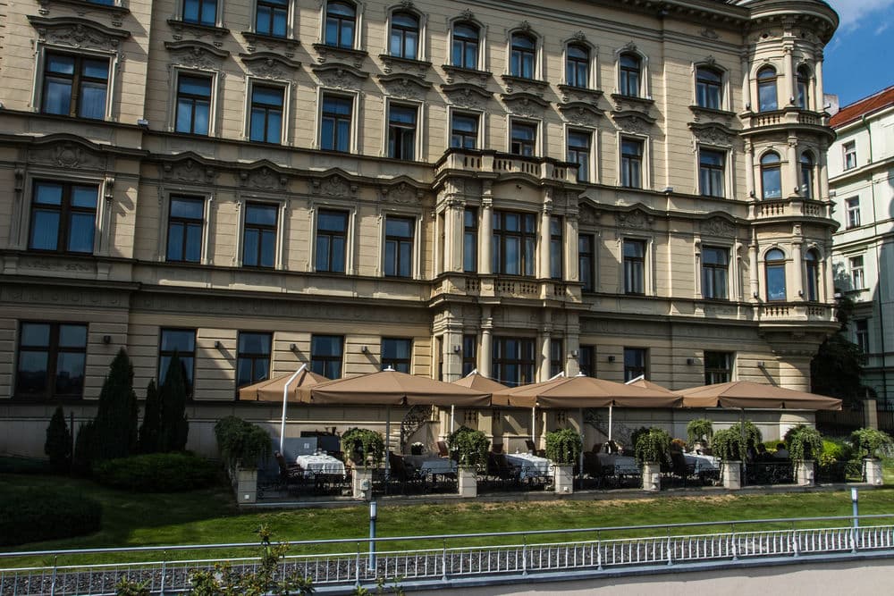 A dramatic, low-angle shot of the Le Palais Art Hotel facade at dusk, highlighting the Belle Époque molding and warm light spilling from the Artista Restaurant terrace.