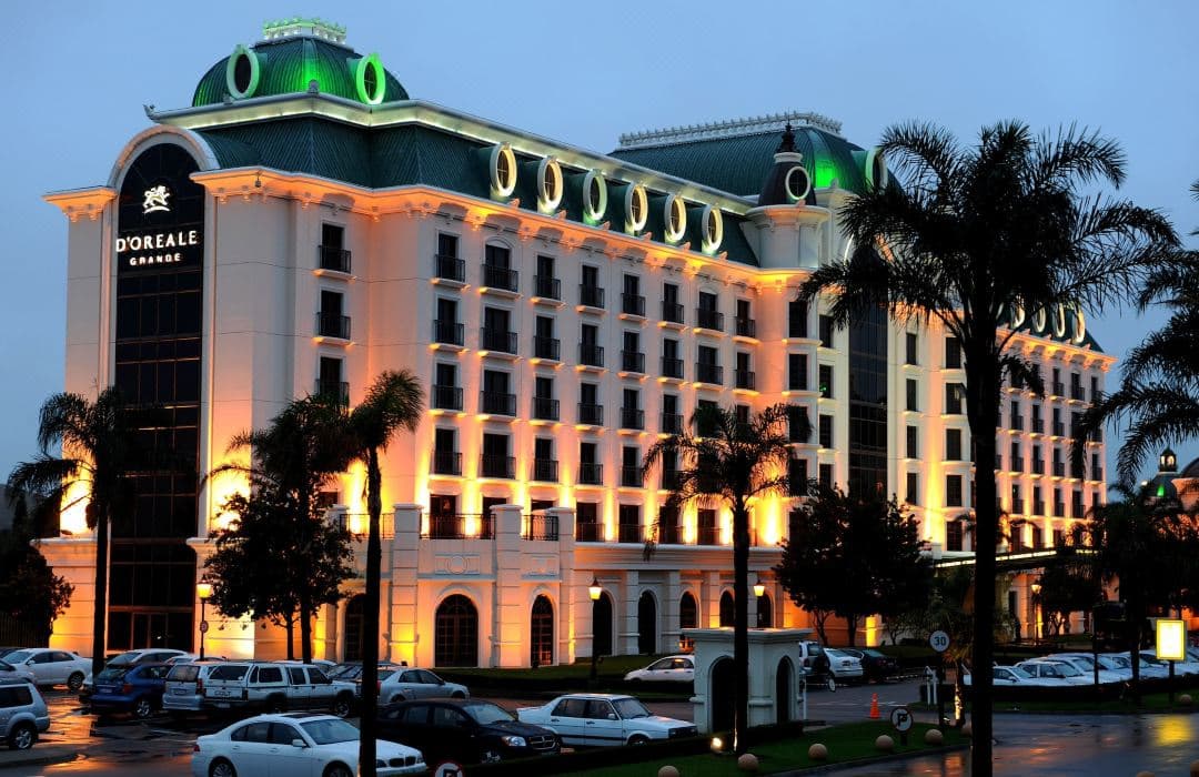 The illuminated Roman-inspired pool deck of Peermont D'oreale Grande at twilight, featuring fountains and palm trees.