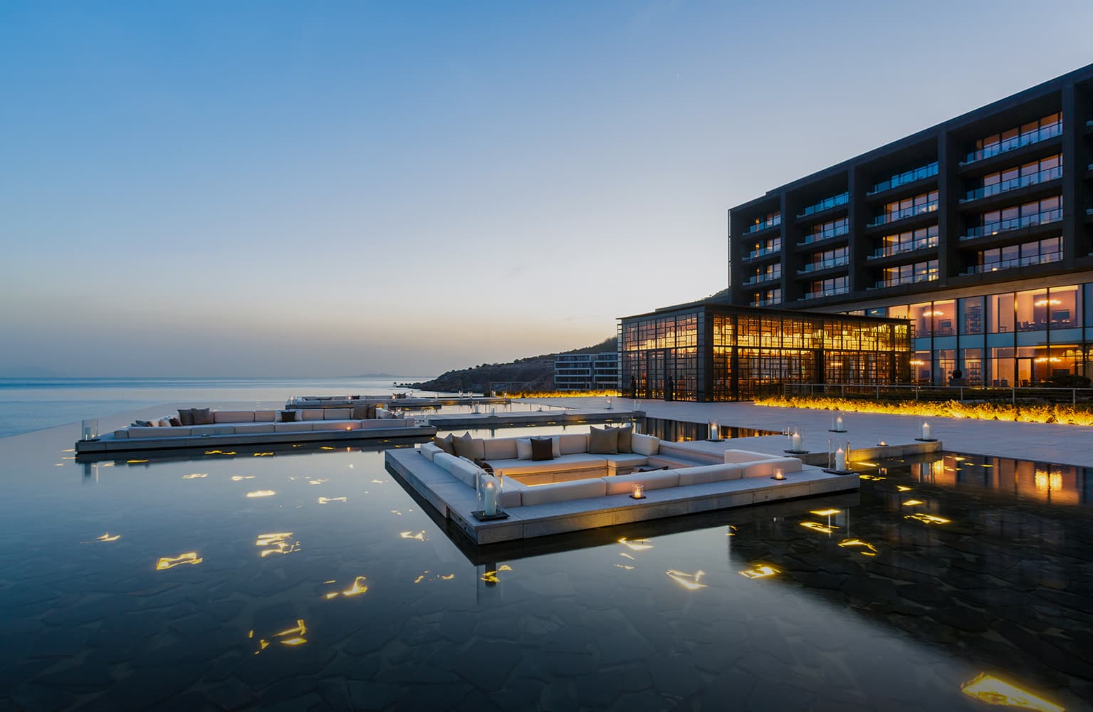 The Lalu Qingdao's signature Mirror Pond reflecting a solitary tree against the backdrop of the Yellow Sea and Kerry Hill's minimalist stone architecture.