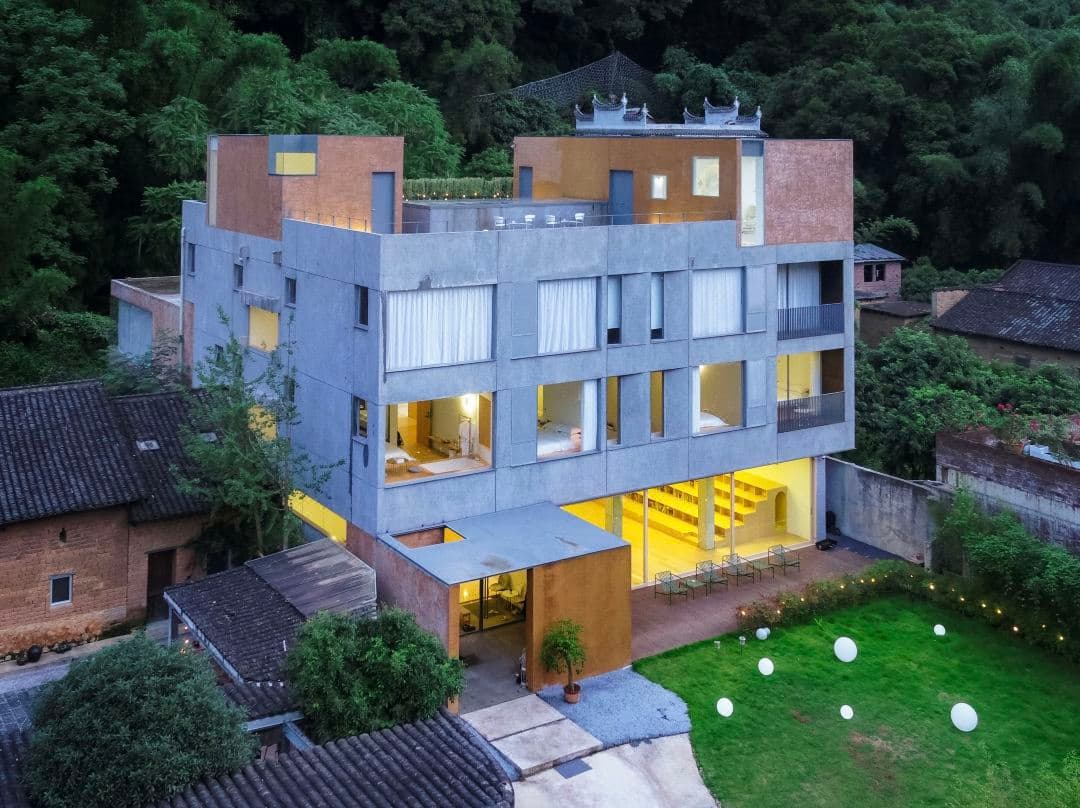 A dramatic brutalist concrete hotel facade featuring a giant silver slide spiraling through the atrium, set against lush green Karst mountains in Yangshuo.