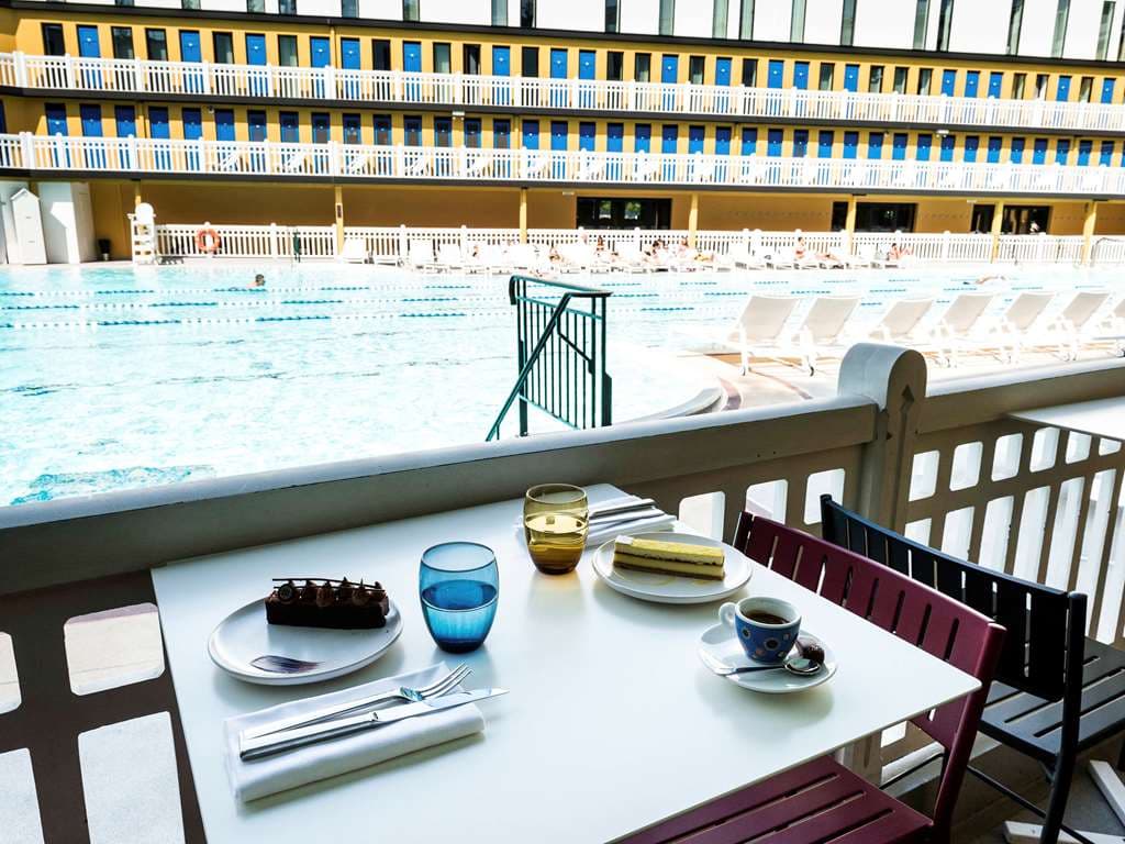 The iconic 46-meter outdoor pool at Molitor Hotel Paris, surrounded by yellow Art Deco balconies and sun loungers under a blue sky.