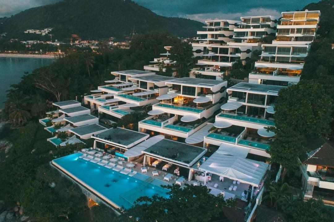 Kata Rocks main 35m infinity pool at sunset with white umbrellas and futuristic white villa terraces overlooking the Andaman Sea.