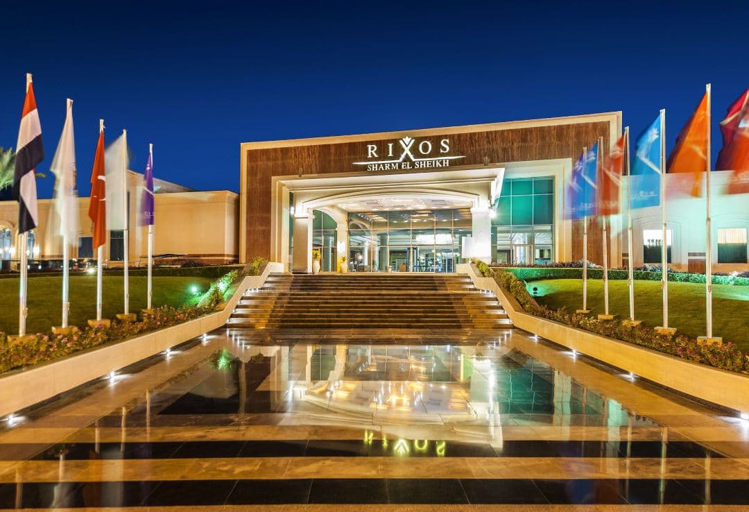 A serene swim-up suite at Rixos Sharm El Sheikh at dusk, featuring a floating breakfast tray and illuminated pool waters reflecting palm trees.