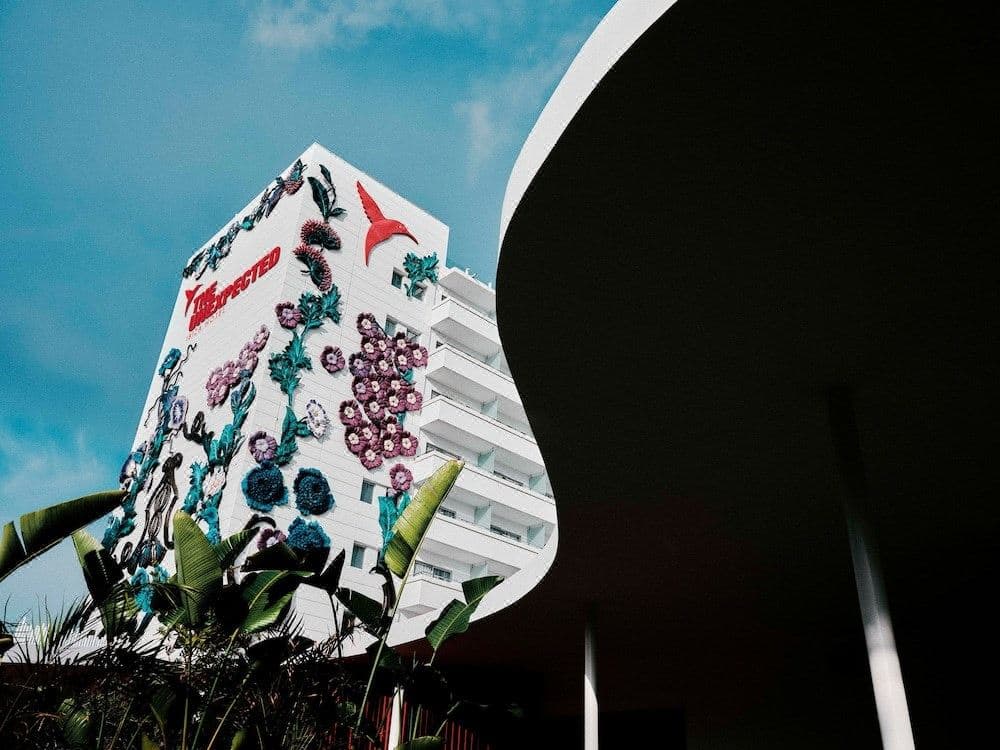 The iconic red pool at Ushuaïa Ibiza Beach Hotel surrounded by white loungers and the main stage, with giant ant sculptures on the building facade.
