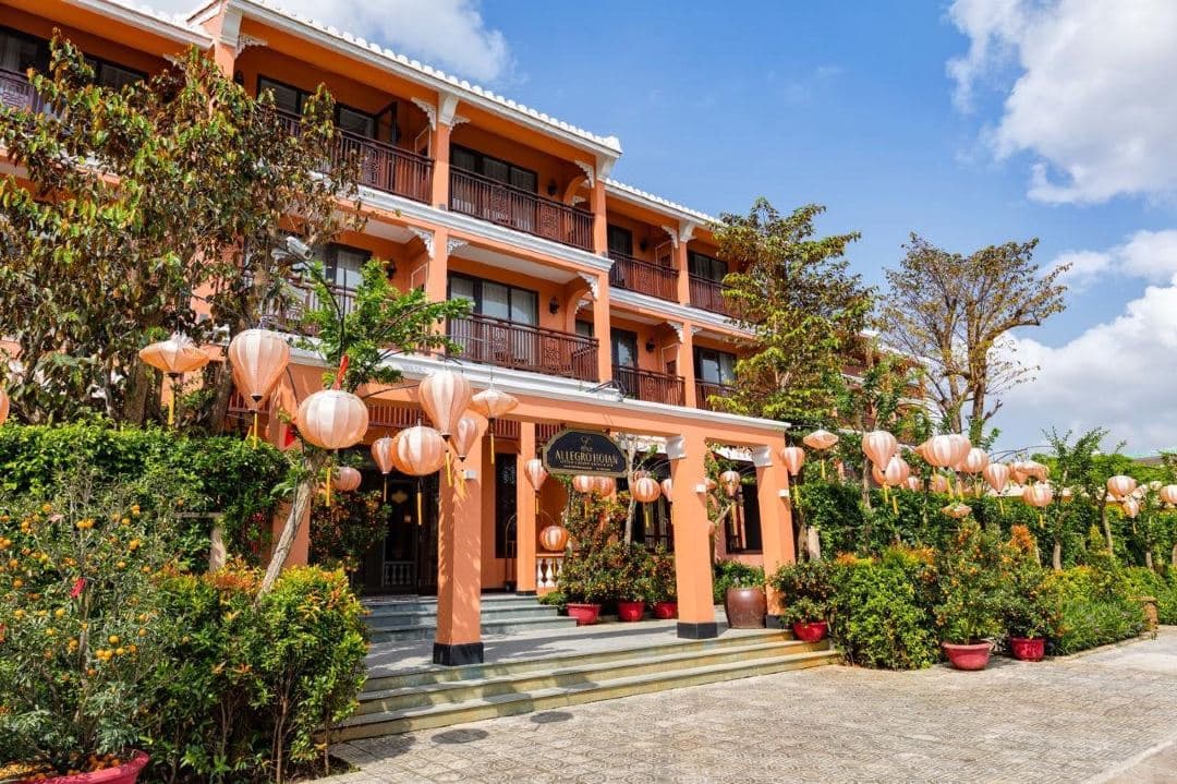 Allegro Hoi An central swimming pool courtyard surrounded by mustard-yellow colonial architecture and wooden balconies.