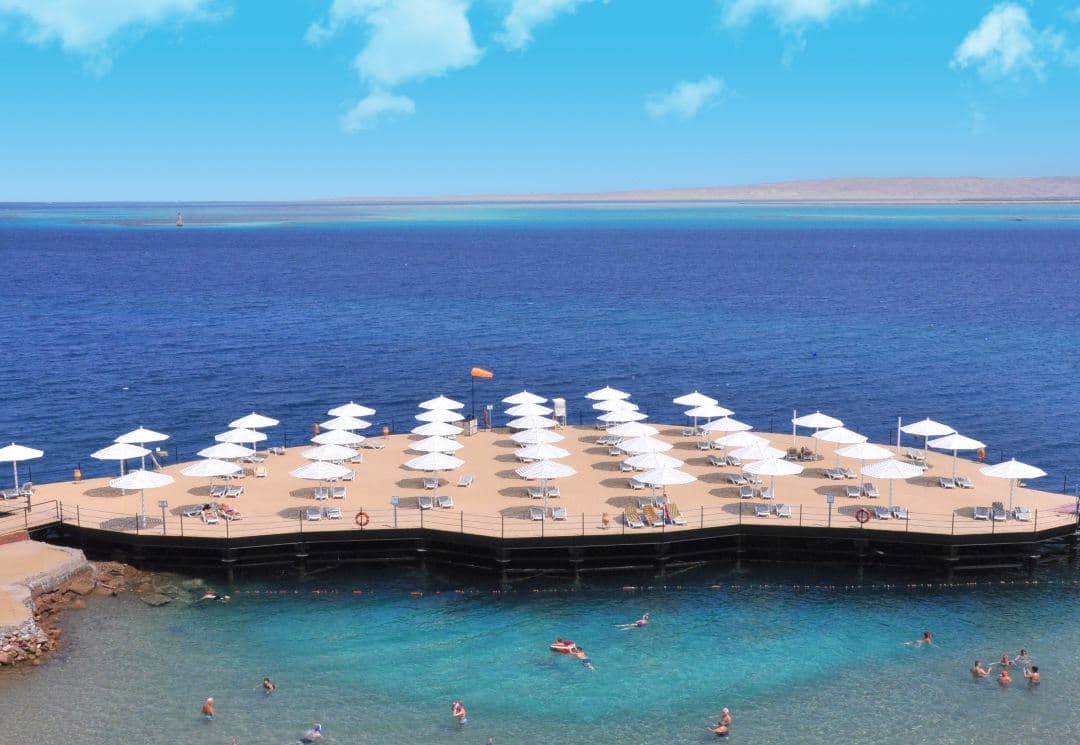 A couple walking hand-in-hand along the Private Island Walkway at SUNRISE Holidays Resort, with the Red Sea lagoon extending into the horizon.