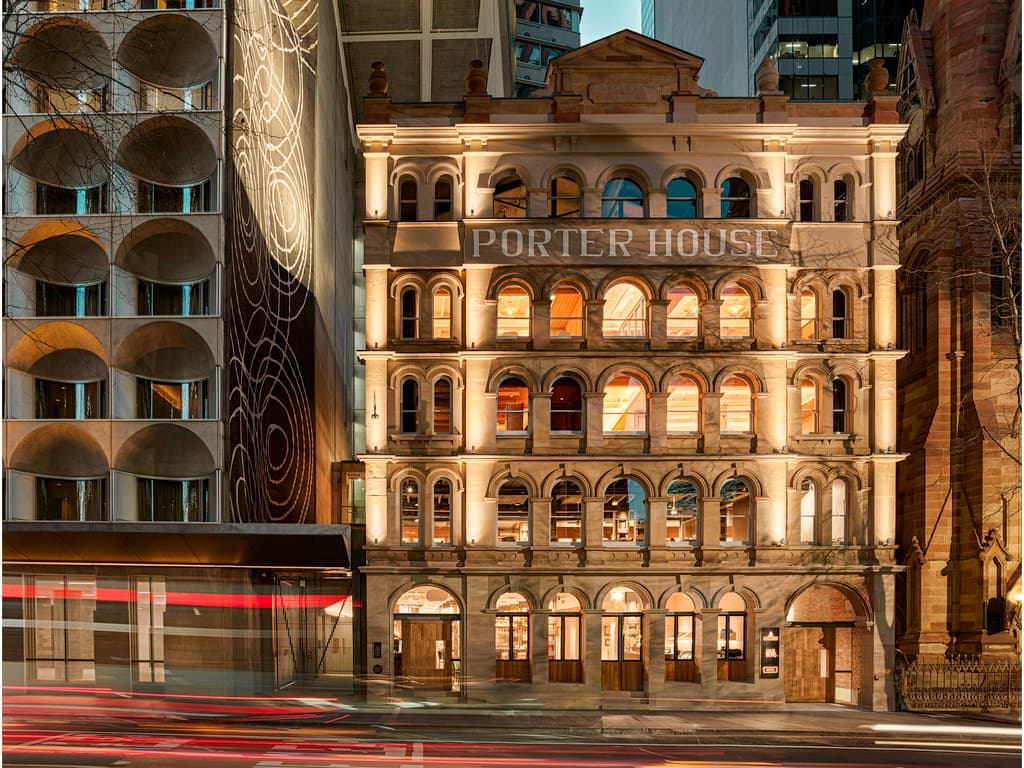 雪梨 Porter House Hotel 的低角度拍攝，顯示連接砂岩古蹟建築與現代深色塔樓的玻璃橋。