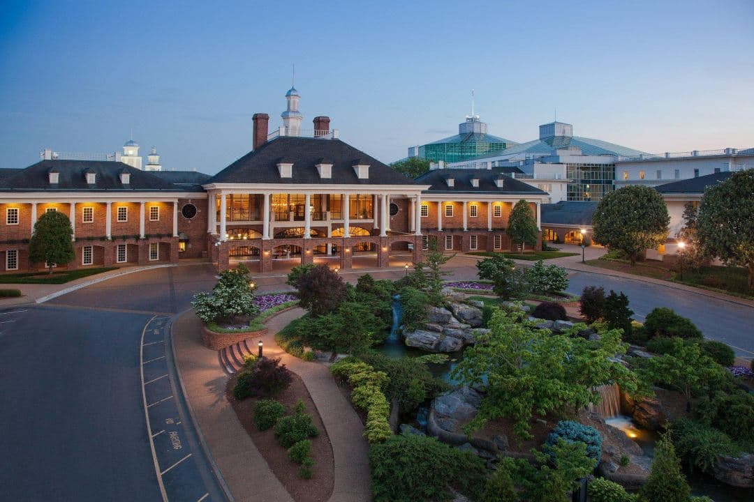 A vast indoor glass atrium at Gaylord Opryland featuring a winding river, lush tropical gardens, and a white gazebo under a steel framework ceiling.
