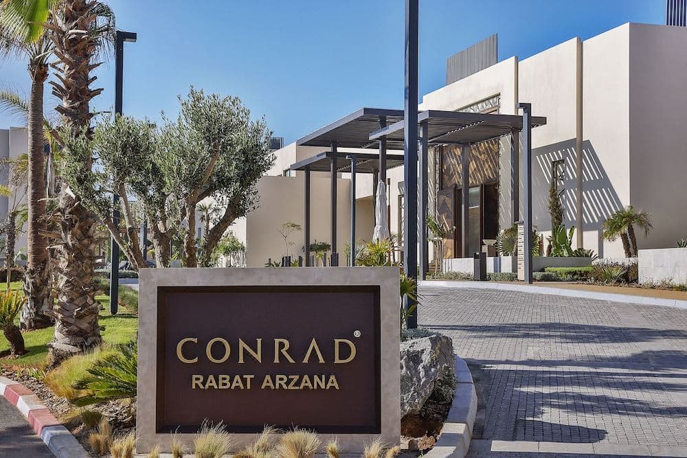 Conrad Rabat Arzana lobby arch framing the Atlantic Ocean sunset with modern white architecture.