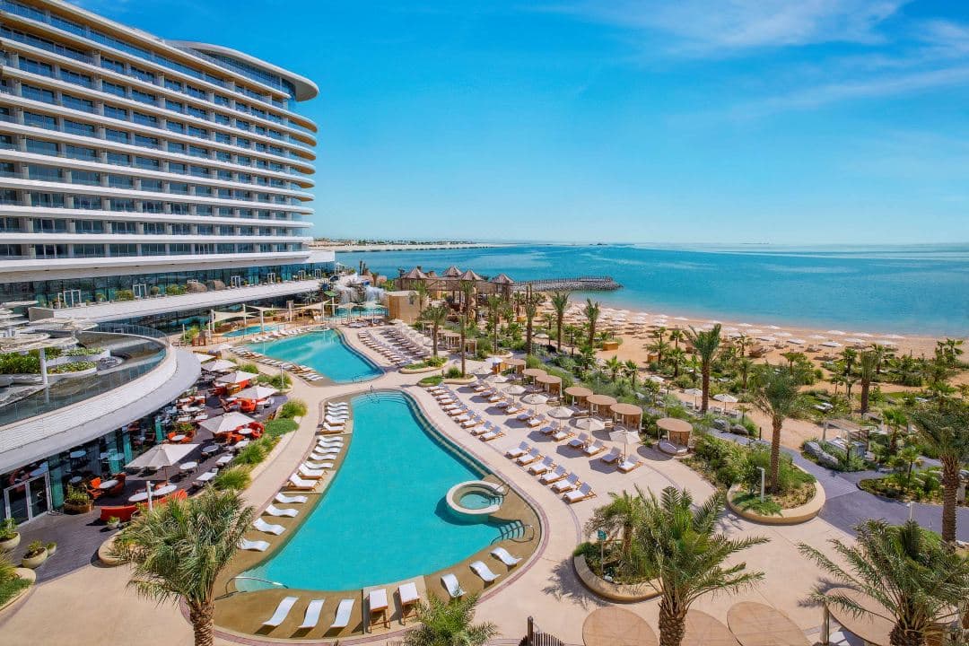 The sweeping white curves of the Waldorf Astoria Lusail Doha exterior against the blue Persian Gulf, featuring the private beach and pool deck.