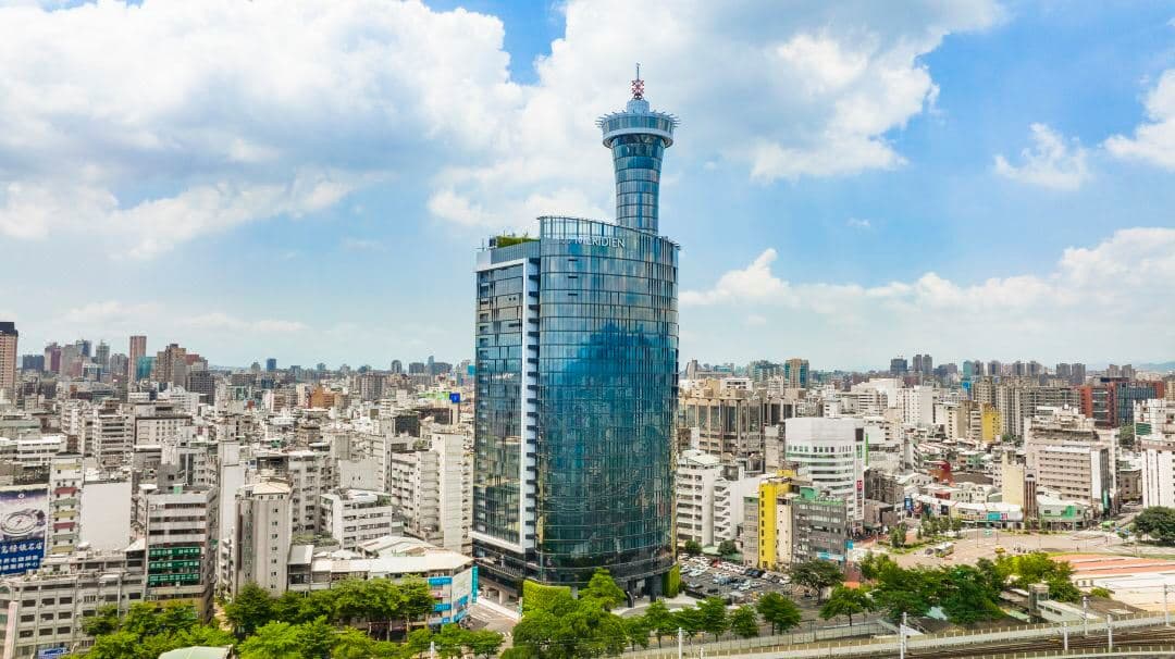 A sleek, modern hotel room at Le Méridien Taichung featuring floor-to-ceiling windows overlooking the city skyline and train station.