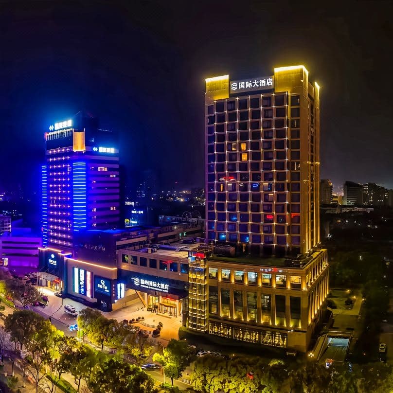 Wenling International Hotel exterior at twilight showing the illuminated glass facade against the traffic of Sanxing Avenue.