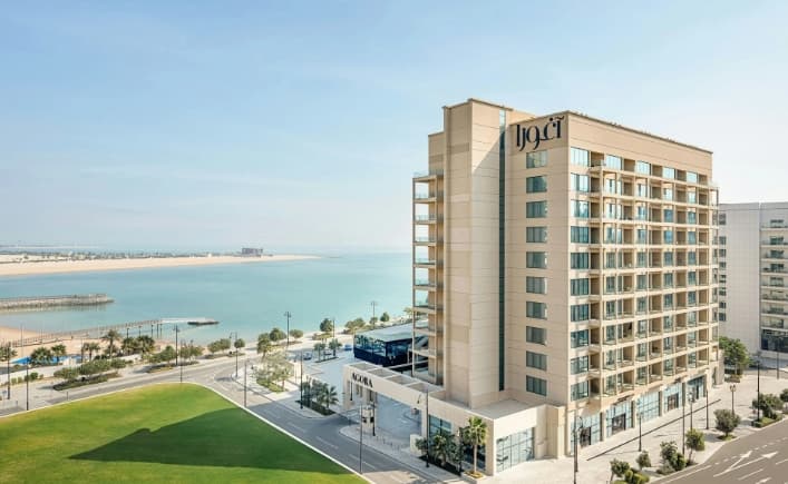 Rooftop infinity pool at Agora Doha with guests lounging on white chaises against the Lusail skyline.
