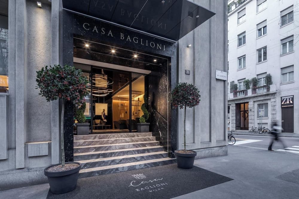 Lobby of Casa Baglioni Milan featuring geometric neon Panzeri chandeliers and 1960s-inspired Spotti Milano furniture with a terrazzo floor.