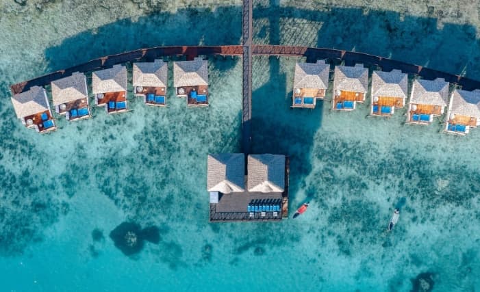 A wooden jetty at Le Mersenne Zanzibar extending into turquoise waters, with a couple relaxing on the Ocean Edge Swing at sunset.