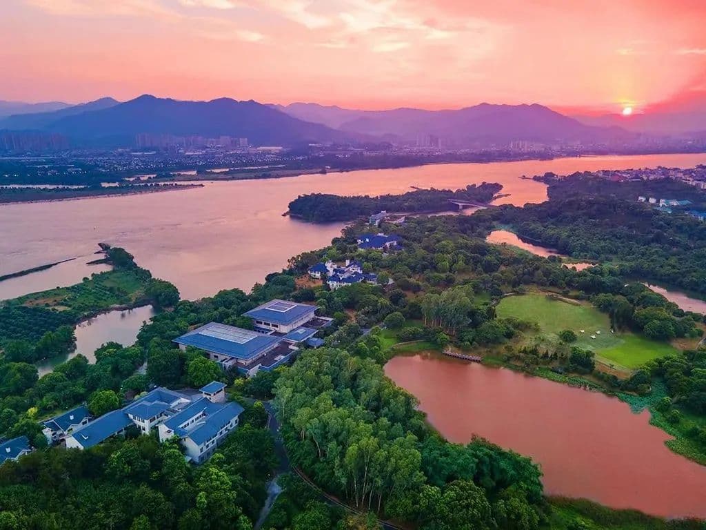 Sunset over the Wolong Covered Bridge at Carp Islet Resort, reflecting orange light onto the Min River wetlands.