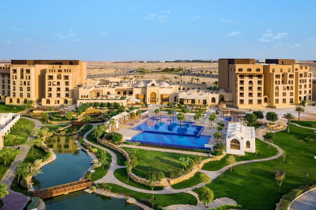 A sprawling infinity pool at InterContinental Durrat Al Riyadh bordered by palm trees and lush gardens, reflecting the resort's distinct architecture.