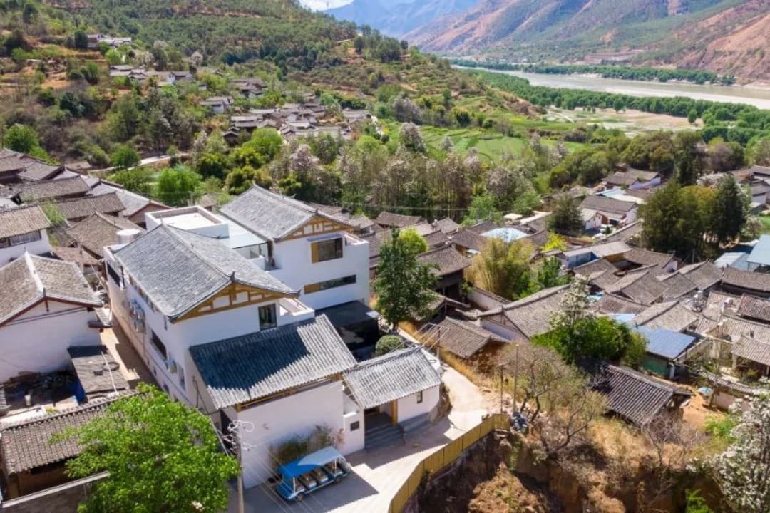 A serene view from a LUX* Sangushui suite balcony featuring traditional Naxi tiled rooftops against the backdrop of the Jinsha River and misty mountains.