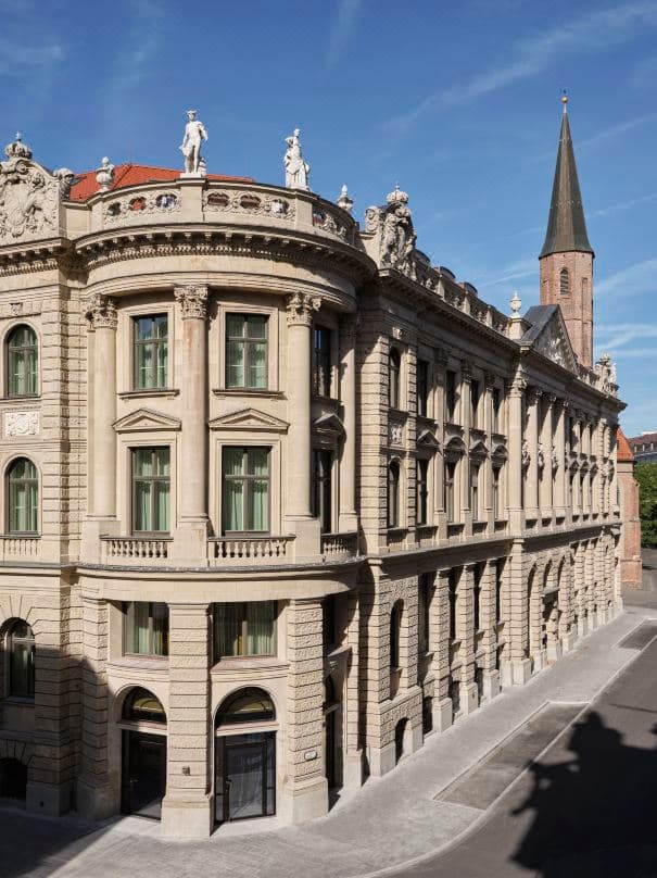 The grand baroque facade of Rosewood Munich illuminated at twilight, featuring the historic entrance of the former State Bank of Bavaria.