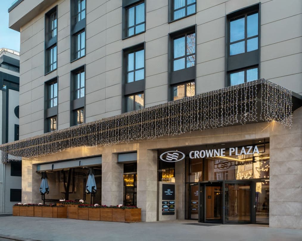 View from Crowne Plaza Ortakoy balcony showing the illuminated Bosphorus Bridge and Ortakoy Mosque at twilight.