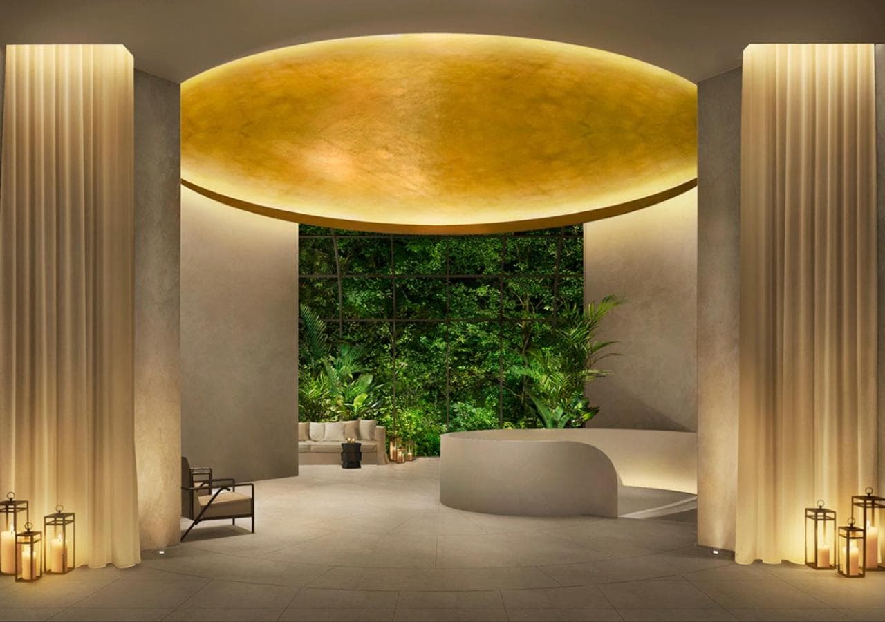 The Singapore EDITION lobby featuring a white spiral staircase surrounded by lush indoor tropical plants and white marble flooring.