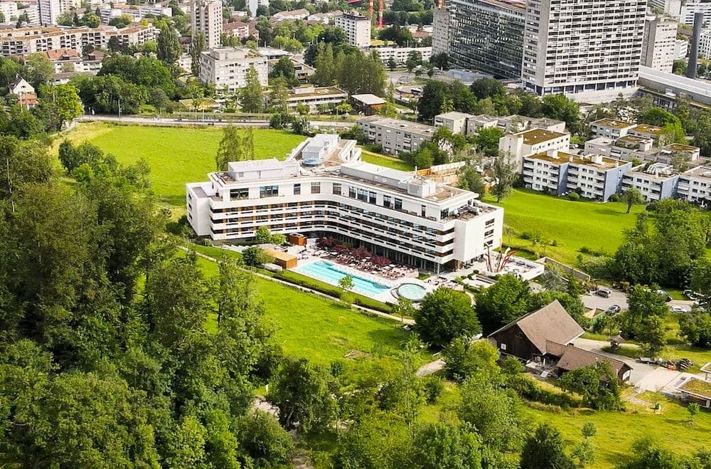 Guests mingling by the glass-walled Social Pool at FIVE Zurich, overlooking the city skyline and Uetliberg forest.