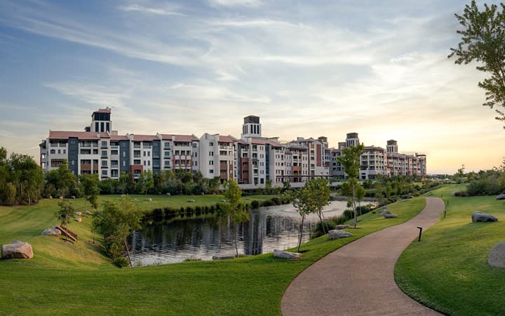 A vast, crystal-clear 300m swimming lagoon surrounded by manicured lawns and modern apartment-style hotel buildings under a bright Johannesburg sky.