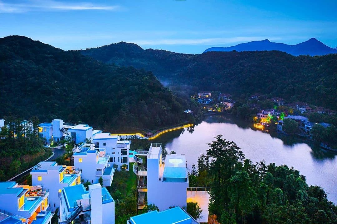 A dramatic side view of a glass-bottomed swimming pool suspended 33 meters in the air over a lush green bamboo valley in Moganshan.