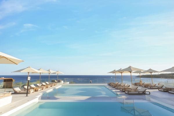 A stark white minimalist resort building contrasting against the deep blue Red Sea sky, with an infinity pool in the foreground.
