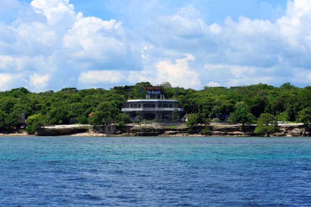 A solitary wooden villa at Plataran Menjangan Resort surrounded by mangroves, overlooking a calm blue ocean with a deer grazing nearby.