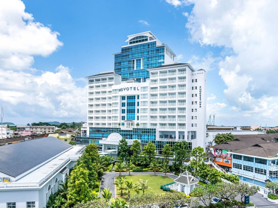 プーケット・オールドタウンのスカイラインと遠くの山々を見渡しながら、Estrela Rooftop Barのテラスでカクテルを楽しむゲスト。
