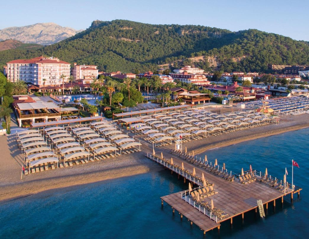 Wooden pier at Akka Alinda Hotel stretching into the turquoise Mediterranean, backed by the pine-covered Taurus Mountains.