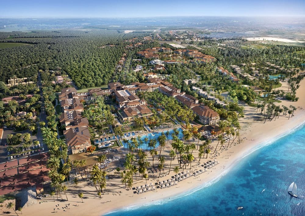 Lopesan Costa Bávaro 巨大的 W 形無邊際泳池在暮色中倒映著棕櫚樹和現代度假村建築。