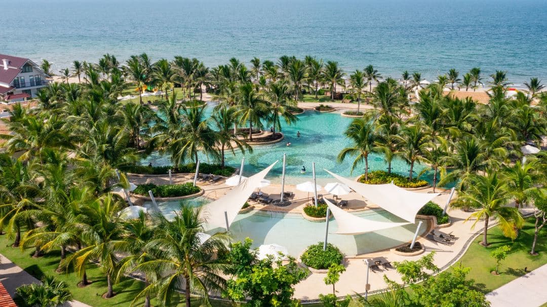 Aerial view of the massive 1,600 sqm swimming pool at Citadines Pearl Hoi An during sunset, bordering the white sands of An Bang Beach.