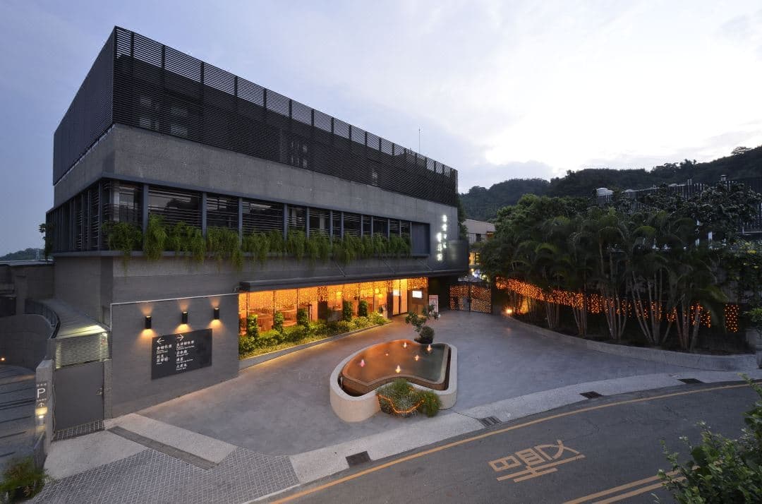 A private in-room hot spring tub at The Sun Hot Spring & Resort made of dark stone, filled with steaming water, overlooking the misty green mountains of Taichung.